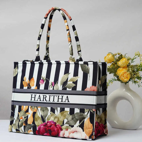 Floral and striped tote bag with 'HARITHA' branding next to a vase with flowers on a light background