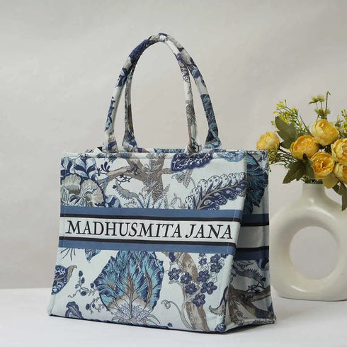 Floral patterned tote bag with 'MADHUSMITA JANA' branding next to a vase with flowers on a white background